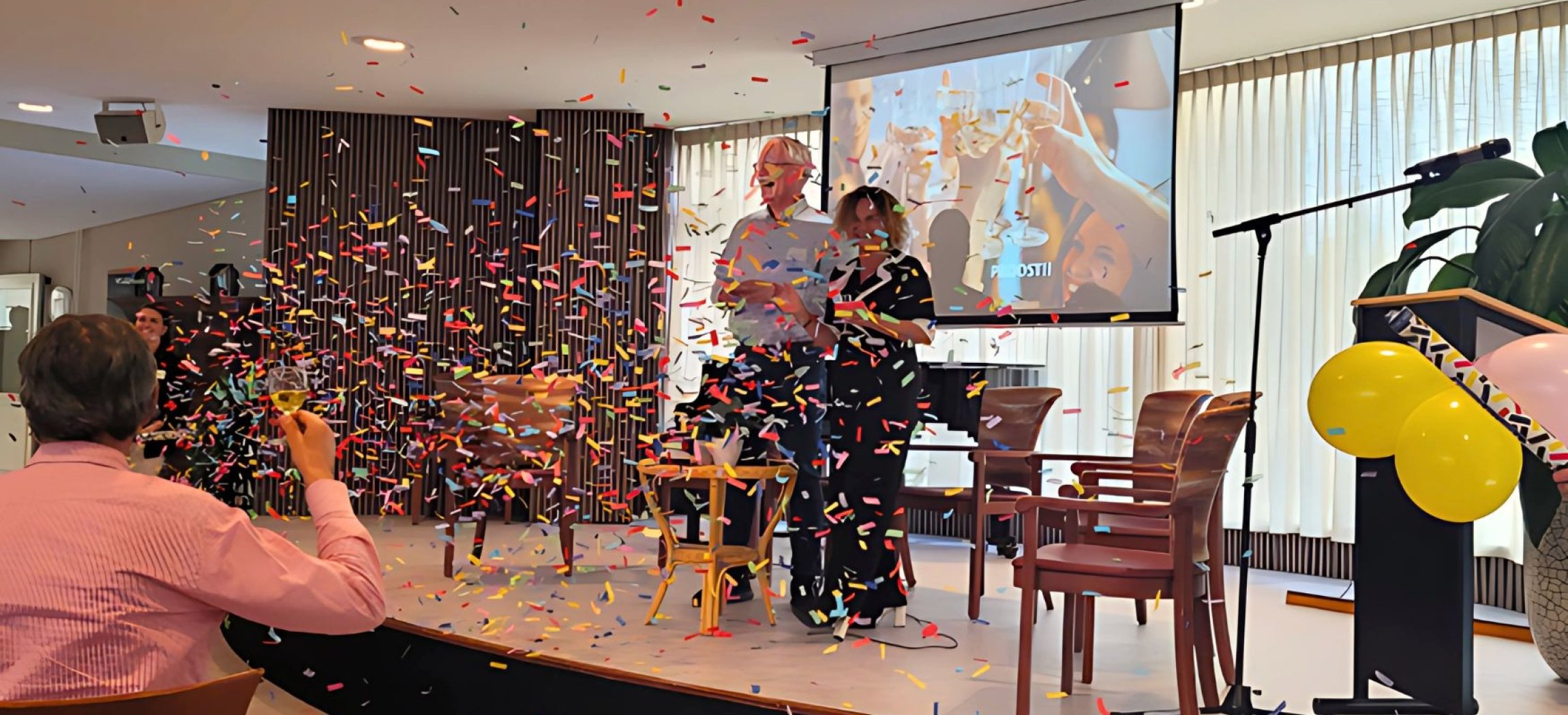Feestelijke opening van het Centraal Aanmeldpunt Wijkzorg met twee personen die een presentatie geven en confetti