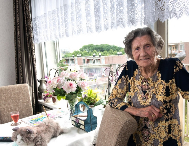 Trotse stoere oudere dame staat in haar woonkamer met tafel tafelkleed gordijnen