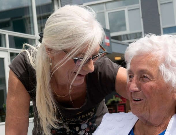Zorgzame vrouw omarmt oudere vrouw met zilverwit haar