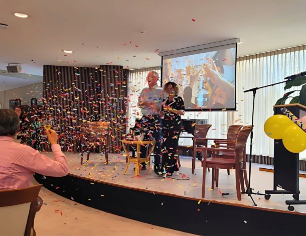 Feestelijke opening van het Centraal Aanmeldpunt Wijkzorg met twee personen die een presentatie geven en confetti
